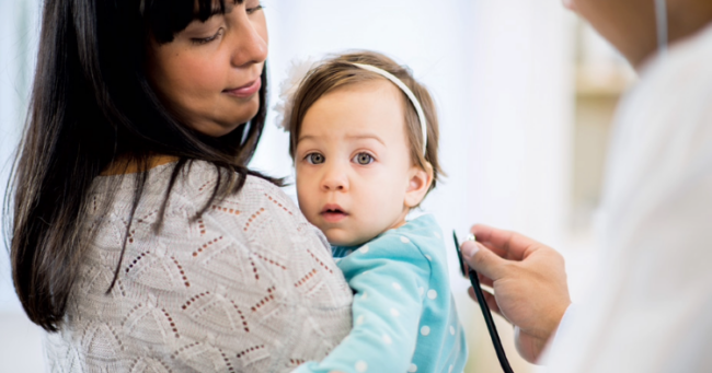 Woman holding a baby with a doctor putting stethoscope to the baby's back.